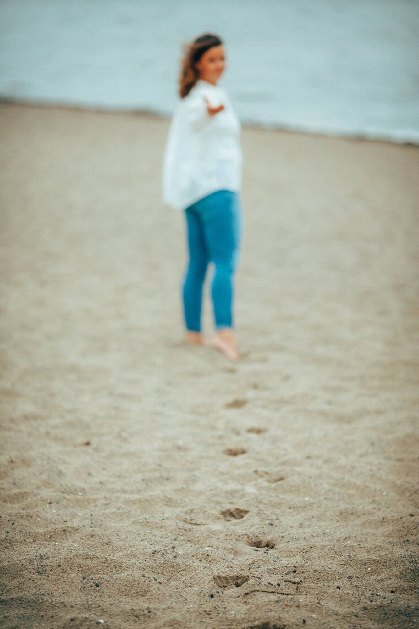 Julia barfuß am Sandstrand vor dem Meer, in weicher Unschärfe