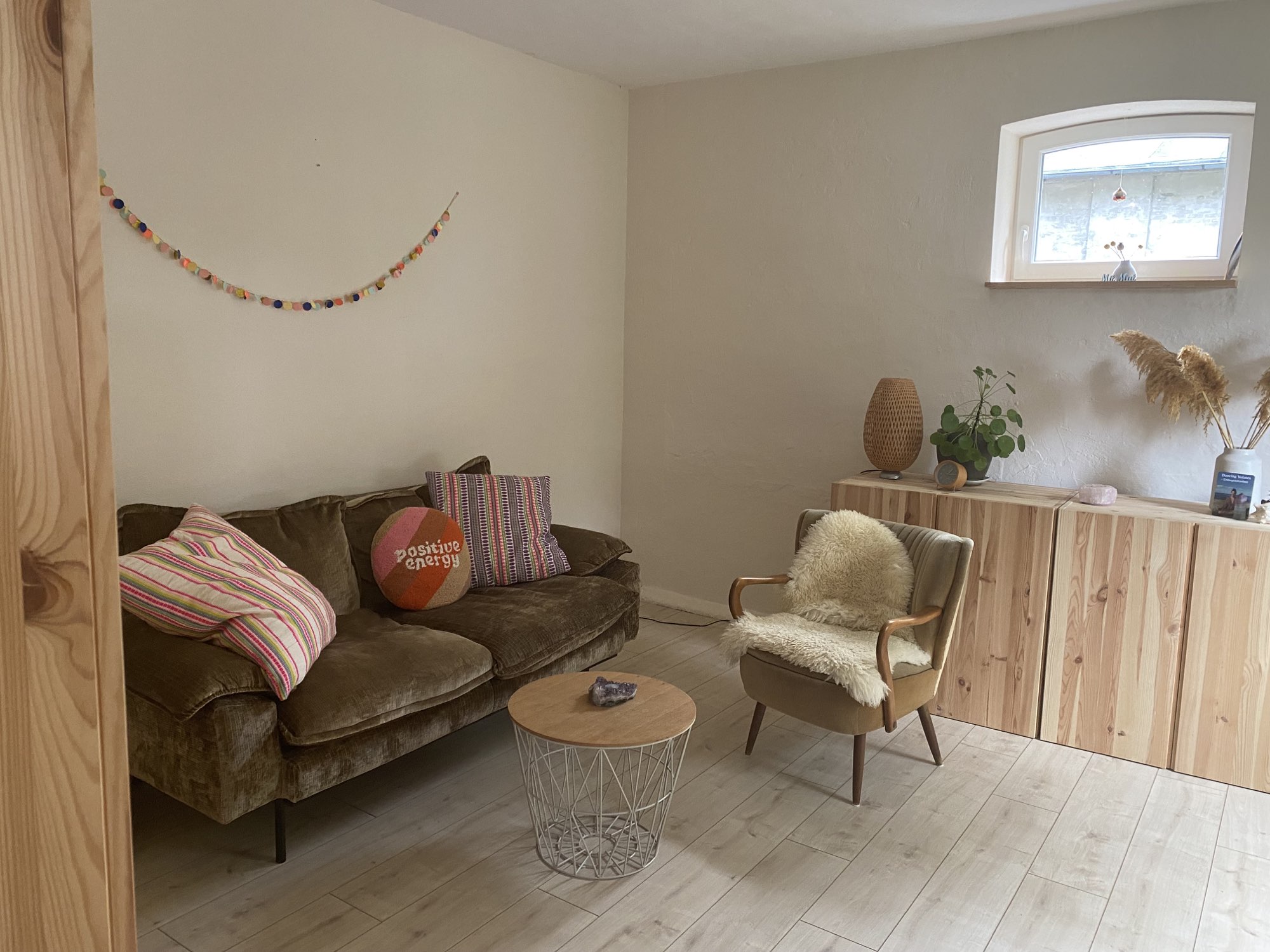 Julias Praxisraum: Sofa mit bunten Kissen, Sessel mit Schaffell und helles Holz